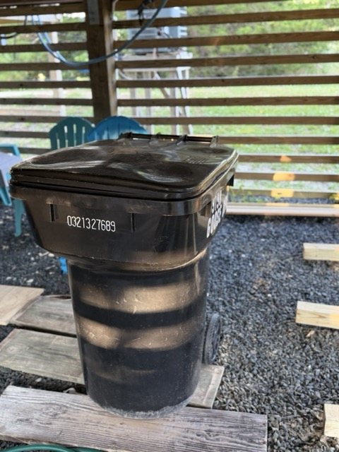 The black wheeled trash can stored under the house
